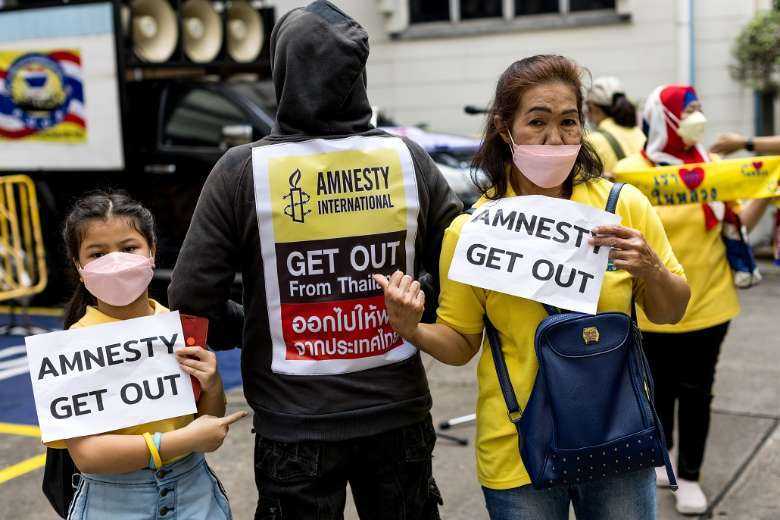 Thai royalists hold signs during a demonstration in Bangkok on Nov. 25, 2021, calling for Amnesty International to stop operations in Thailand for supporting detained political activists held on royal defamation charges