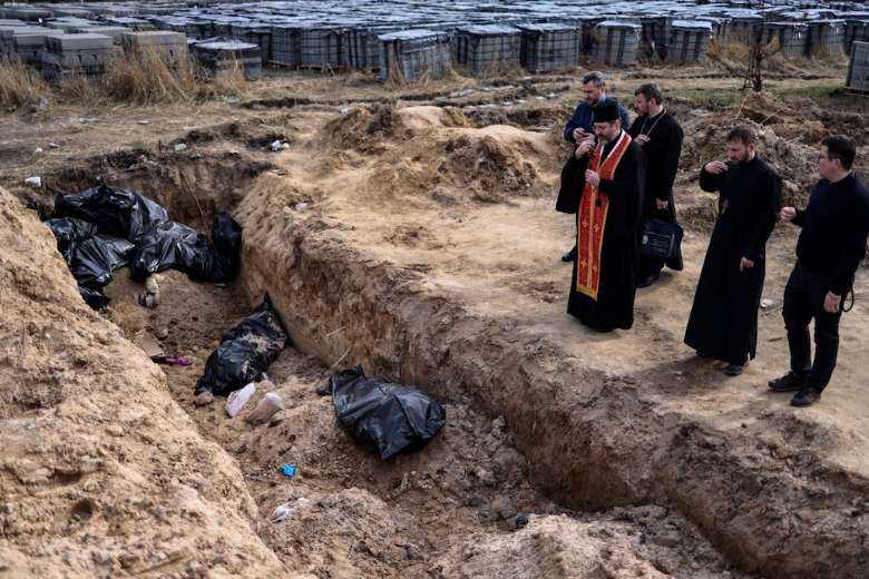 Priests pray before a mass grave in the grounds surrounding St. Andrew's Church in Bucha, Ukraine, on April 7, amid Russia's military invasion