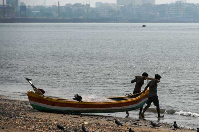 Fishermen pull a boat toward the sea during a hazy day in Mumbai on Nov. 16, 2021