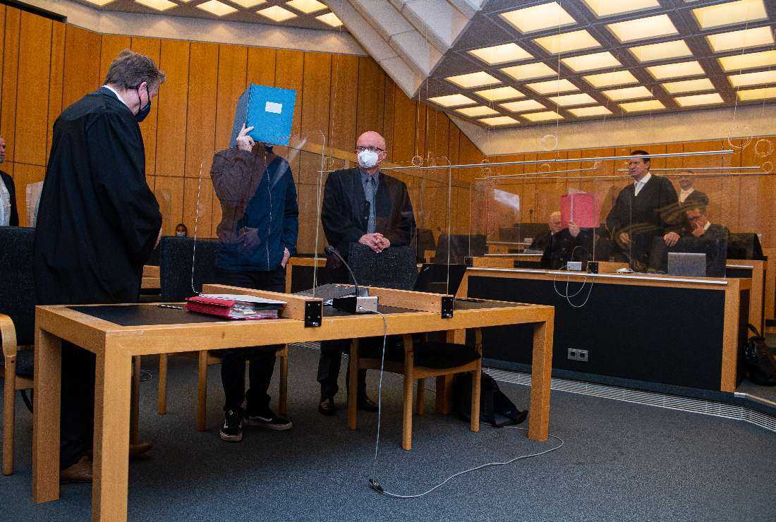 The main defendant standing between his lawyers hides his face behind a folder as he arrives for his judgment in a child sex abuse case at court in Muenster, northwest Germany, on July 6, 2021