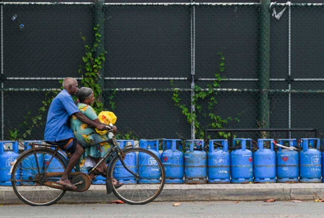 A Sri Lankan couple cycles past a row of liquefied petroleum gas (LPG) cylinders placed by people queueing to buy fuel amid the worst economic crisis, in Galle on July 4