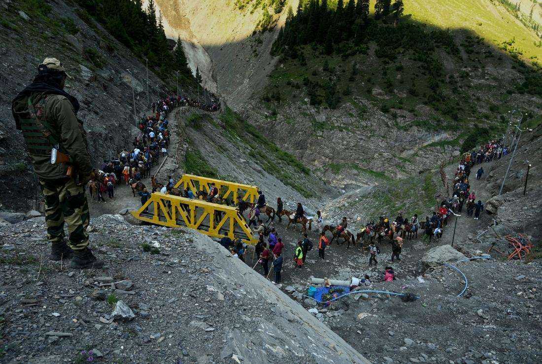 A Border Security Force (BSF) soldier stands guard as Hindu pilgrims cross a bridge during the pilgrimage to the cave shrine of Amarnath from a base camp in Baltal on June 30