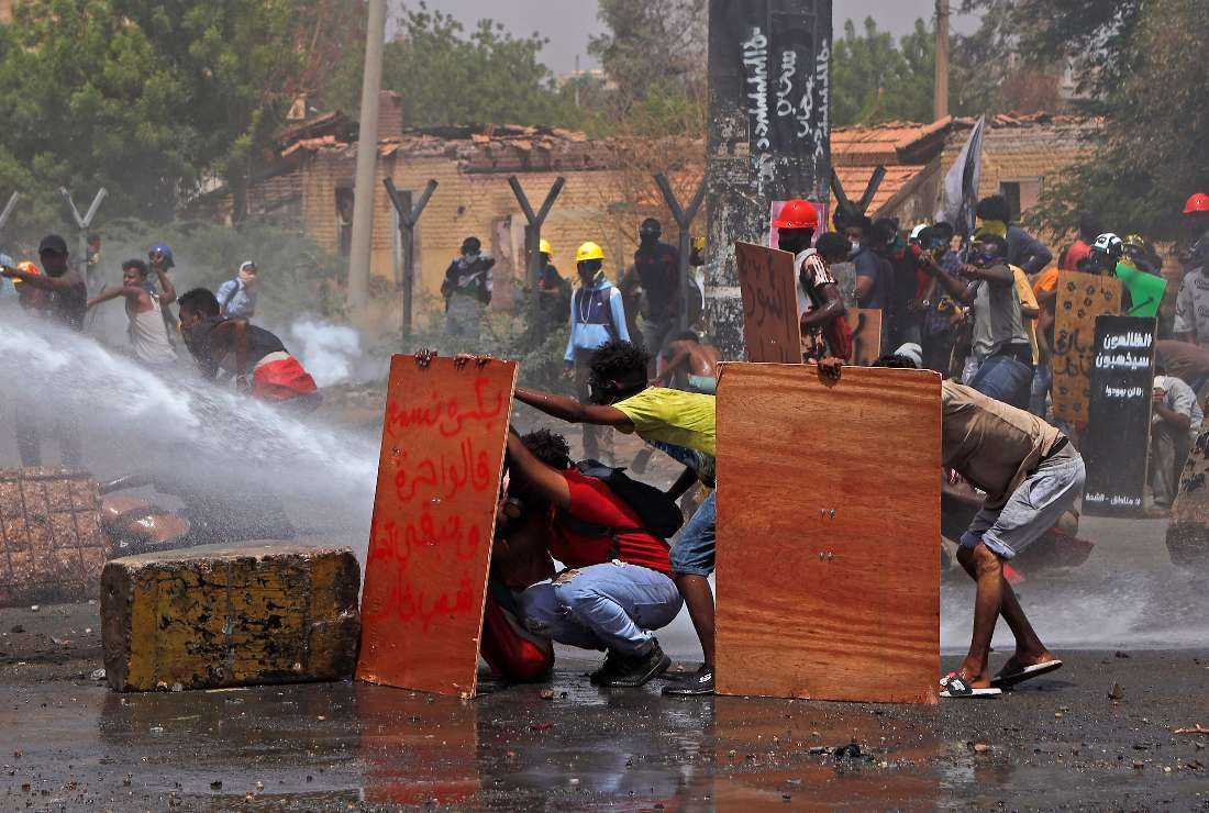 Anti-coup protesters take cover as riot police try to disperse them with water cannon during a demonstration against military rule in the center of Sudan's capital Khartoum on June 30
