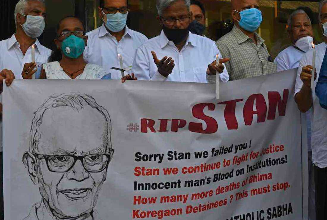 People hold candles and a poster as they pray outside a church holding a memorial Mass for the Indian rights activist and Jesuit priest Father Stan Swamy, in Mumbai on July 6, 2021. He was detained for nine months without trial under Indian anti-terrorism laws and died on July 5 ahead of a bail hearing