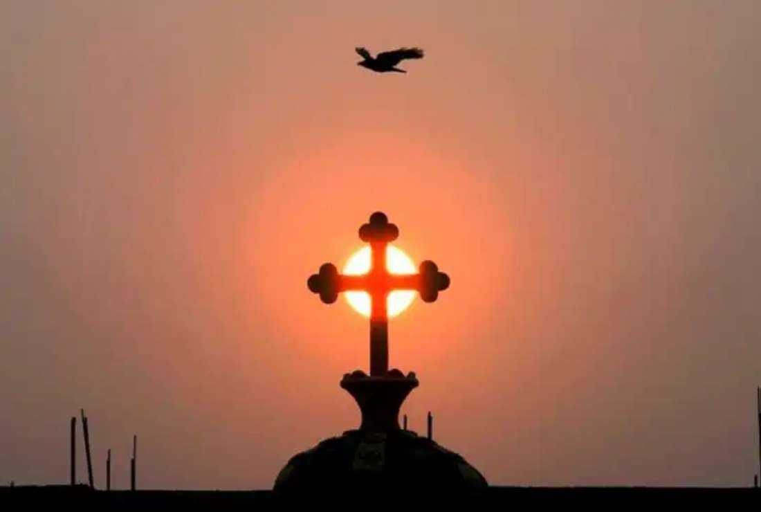 A bird flies over a Christian cross silhouetted against the rising sun on top of a church on the outskirts of Hyderabad, India, on March 12