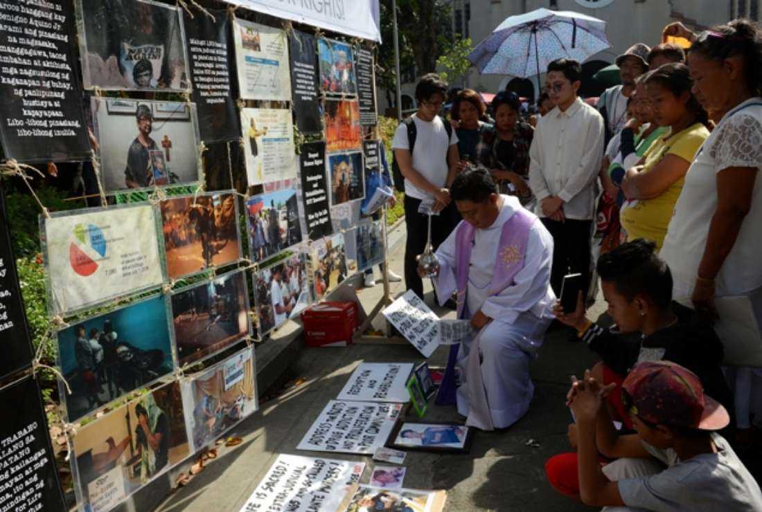A priest blesses photos of victims of extra-judicial killings in President Rodrigo Duterte's drug war during a gathering on the grounds of a church in Manila on March 1, 2017