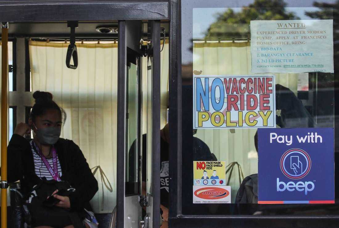 A passenger sits inside a bus next to signage that reads 'No Vaccine No Ride' in Quezon City, suburban Manila on January 17, 2022