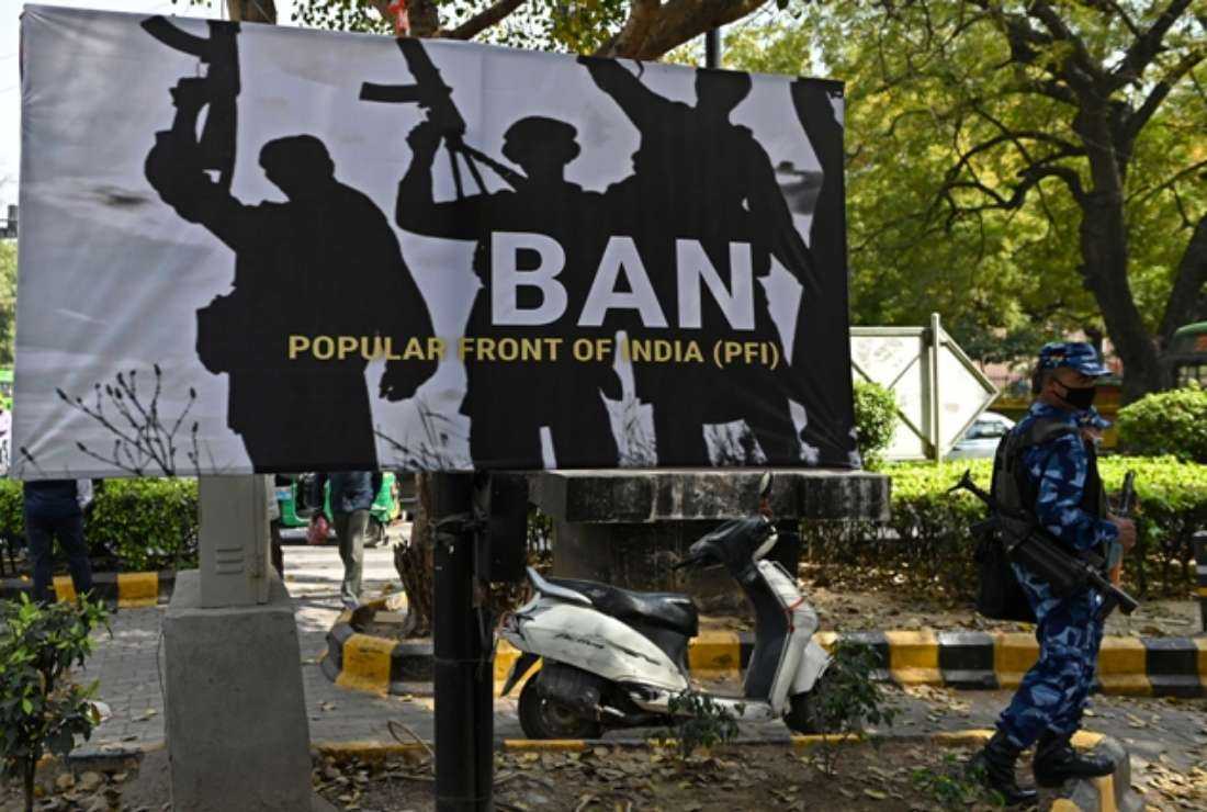 An Indian security officer stands guard beside a banner installed by members of India's ruling Bharatiya Janata Party during a protest demanding a ban on the Popular Front of India in New Delhi on Feb. 28, 2021