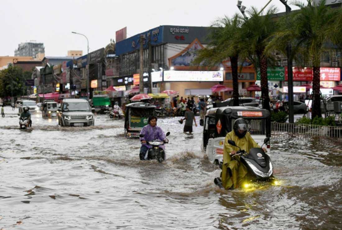 People ride through a flooded street in Phnom Penh, following a heavy rain shower, on Sept. 26