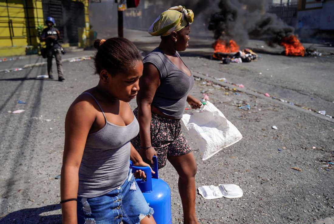 Women carry a container of propane gas during a demonstration to demand the resignation of Prime Minister Ariel Henry and against the charter in Port-au-Prince on Sept. 29