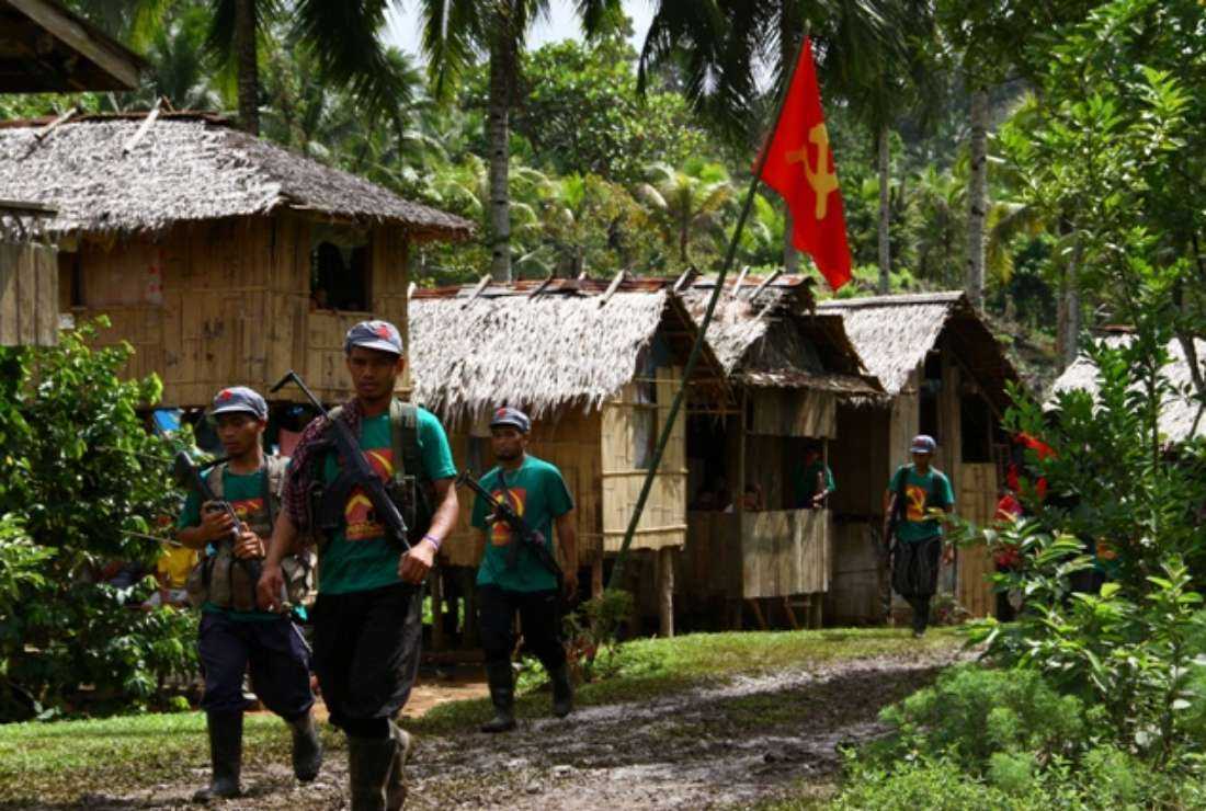 Members of the communists' armed wing, the New People's Army (NPA), walk past a hammer and sickle flag displayed in a village as they mark the 46th anniversary of its founding, on the southern island of Mindanao, on Dec. 26, 2014