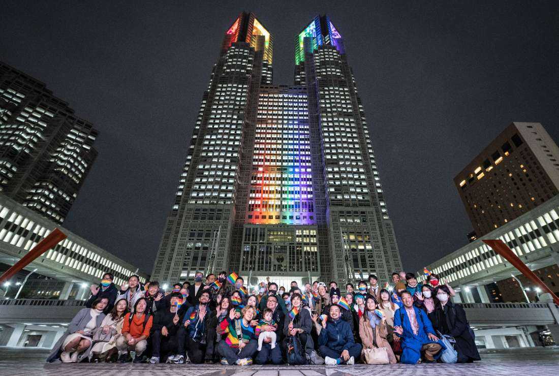 People pose for photographs in front of the Tokyo Metropolitan Government building illuminated with rainbow lights in the Shinjuku district of Tokyo on Nov. 1