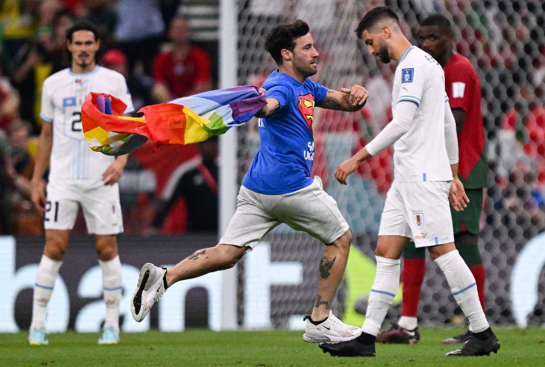 A man invades the pitch holding a LGBT flag as he wears a t-shirt reading Respect for Iranian woman and Save Ukraine during the Qatar World Cup football match between Portugal and Uruguay at the Lusail Stadium in Lusail, north of Doha on Nov. 28