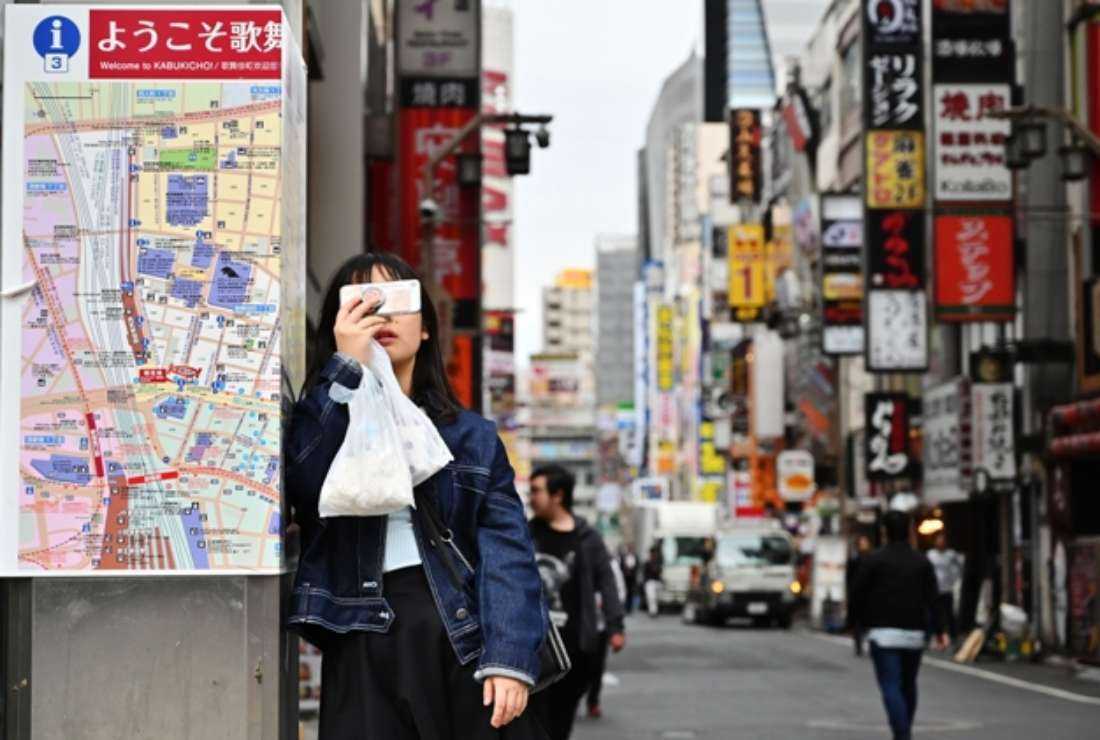 In this photo taken on March 22, 2019, a woman records video footage on her smartphone while standing beside a map in Tokyo's Shinjuku district