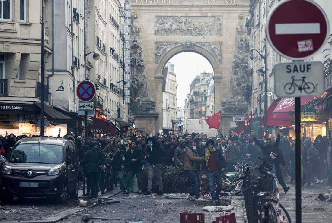 Protestors stand in front of riot police officers at the site where several shots were fired along rue d'Enghien in the 10th arrondissement, in Paris on Dec. 23