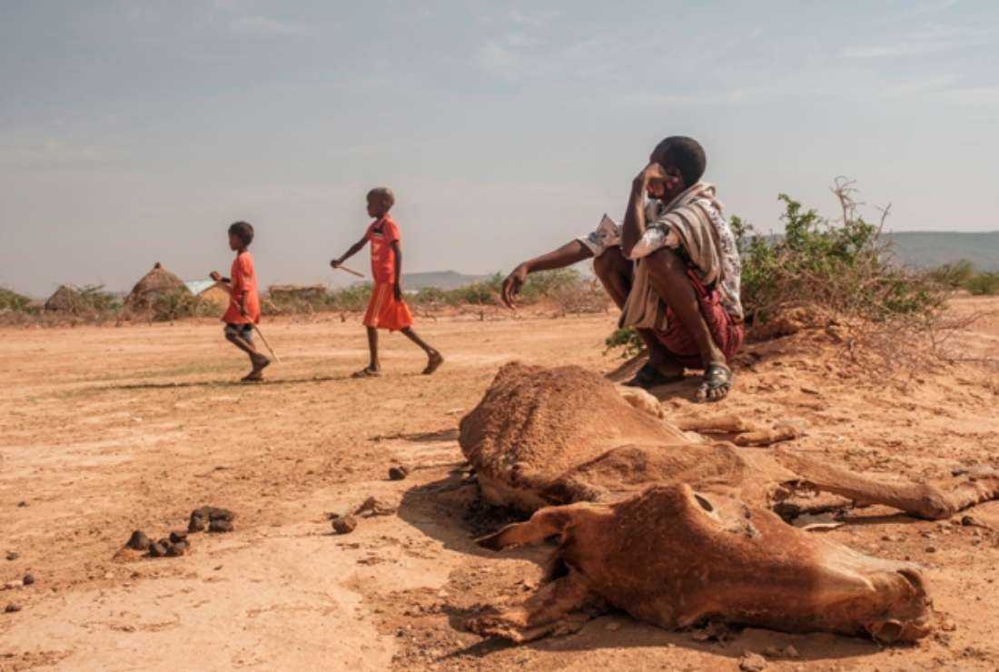 Children walk as a man sits next to the carcass of a dead cow in the village of Hargududo, 80 kilometers from the city of Gode, Ethiopia, on April 07, 2022