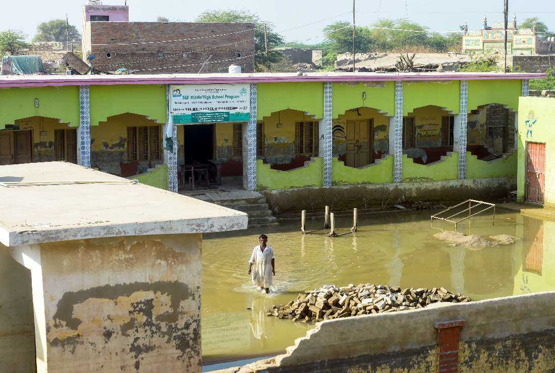 In this picture taken on Oct. 28, 2022, a watchman wades across a flooded school in Chandan Mori, in Dadu district of Sindh province