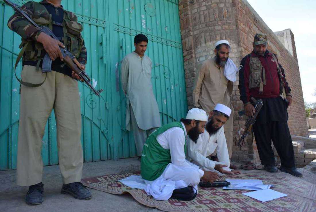 Security personnel stand guard next to an official (center) from the Pakistan Bureau of Statistics, using a digital device to collect information from residents during the first-ever door-to-door digital national census in Bannu, Khyber Pakhtunkhwa province on March 14