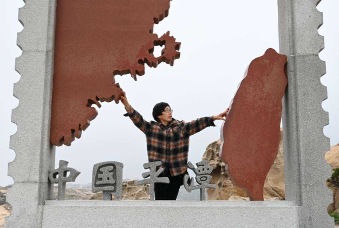 A Chinese tourist poses for photos with an installation depicting Taiwan (right) and mainland China at a tourist area on Pingtan island, the closest point to Taiwan, in China's southeast Fujian province on April 6