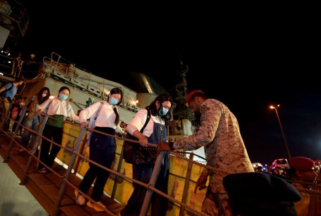 A Saudi Navy sailor assists people evacuated from Sudan upon their arrival at King Faisal Navy base in Jeddah on April 26