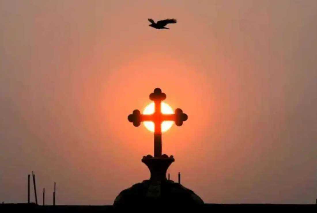 A bird flies over a Christian cross silhouetted against the rising sun on top of a church on the outskirts of Hyderabad, India, on March 12, 2022
