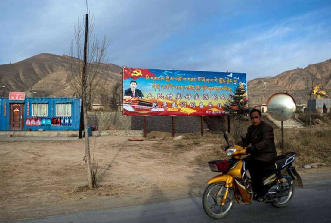 A motorcyclist rides past a propaganda poster showing China's President Xi Jinping, outside Rebgong in China's Qinghai province, March 2, 2018