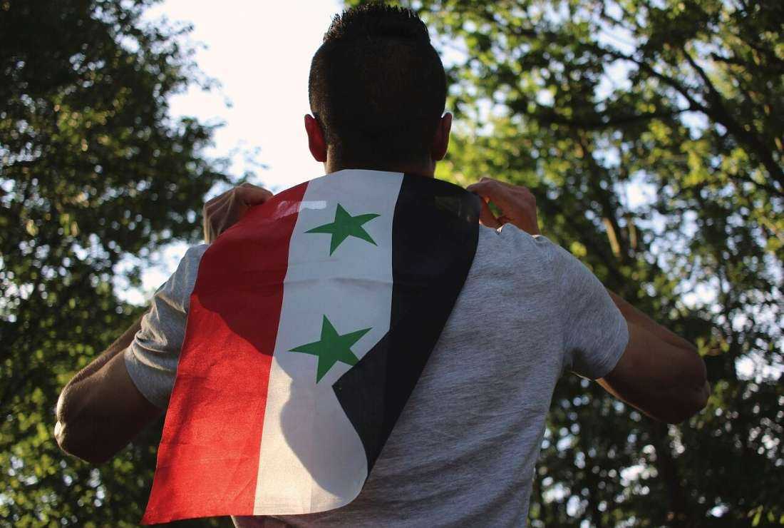 A man is seen holding the Syrian flag on his back
