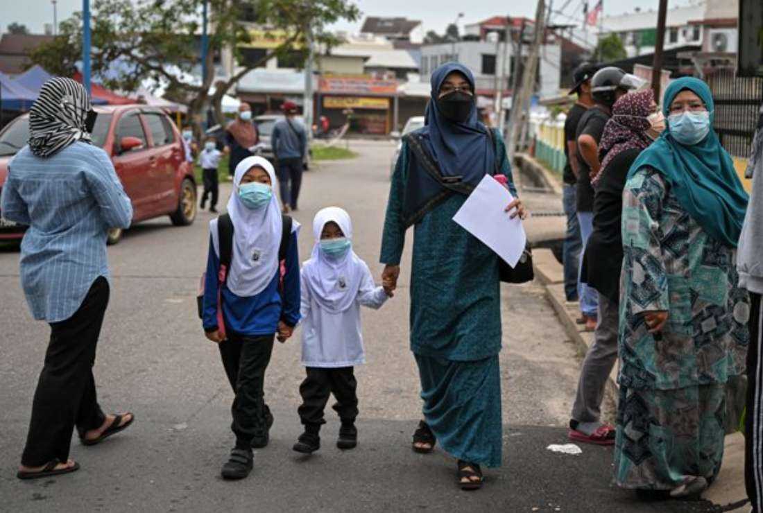 A mother arrives with her daughters on the first day of elementary school in Karak, Malaysia's Pahang state on March 21, 2022