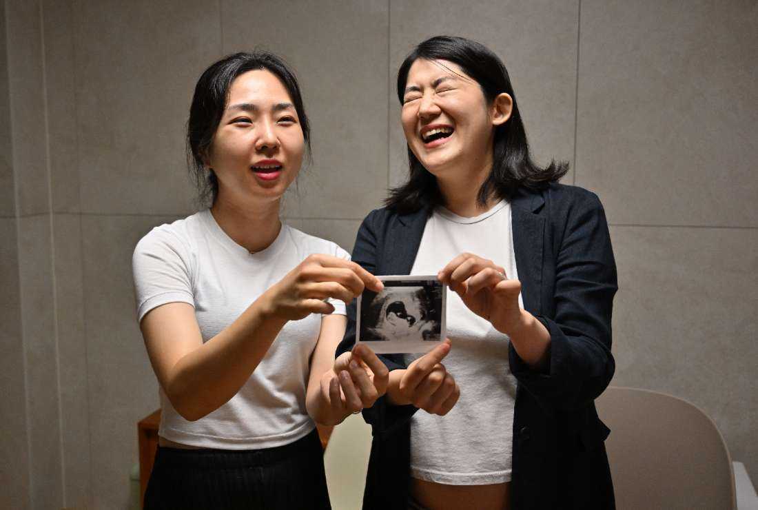 This picture taken on July 18 shows South Korean lesbian couple Kim Kyu-jin (right) and her wife Kim Sae-yeon (left) posing with a fetal ultrasound image during an interview with AFP at their home in Seoul. South Korea has spent billions of dollars on policies to boost its birthrate