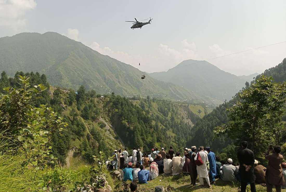 People watch as an army soldier slings down from a helicopter during a rescue mission to recover students stuck in a chairlift in Pashto village of mountainous Khyber Pakhtunkhwa province, on Aug. 22