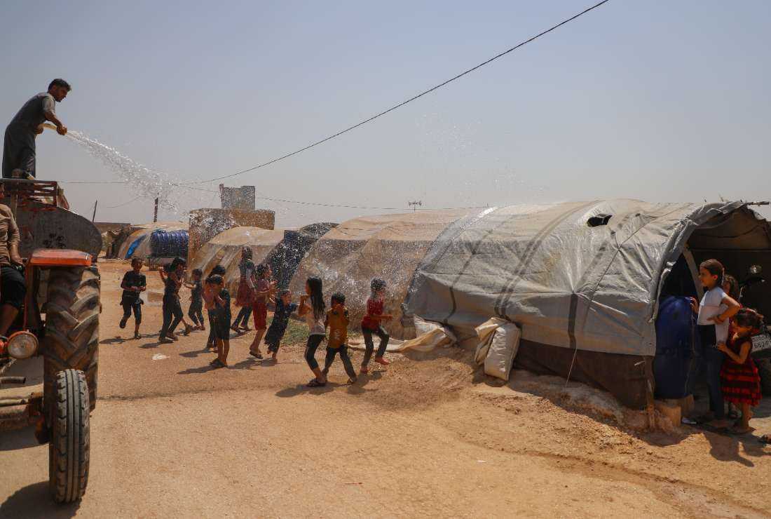 People spray youths with water amid soaring temperatures in a camp for the internally displaced in Zaradna in Syria's rebel-held northwestern Idlib province, on Aug. 14