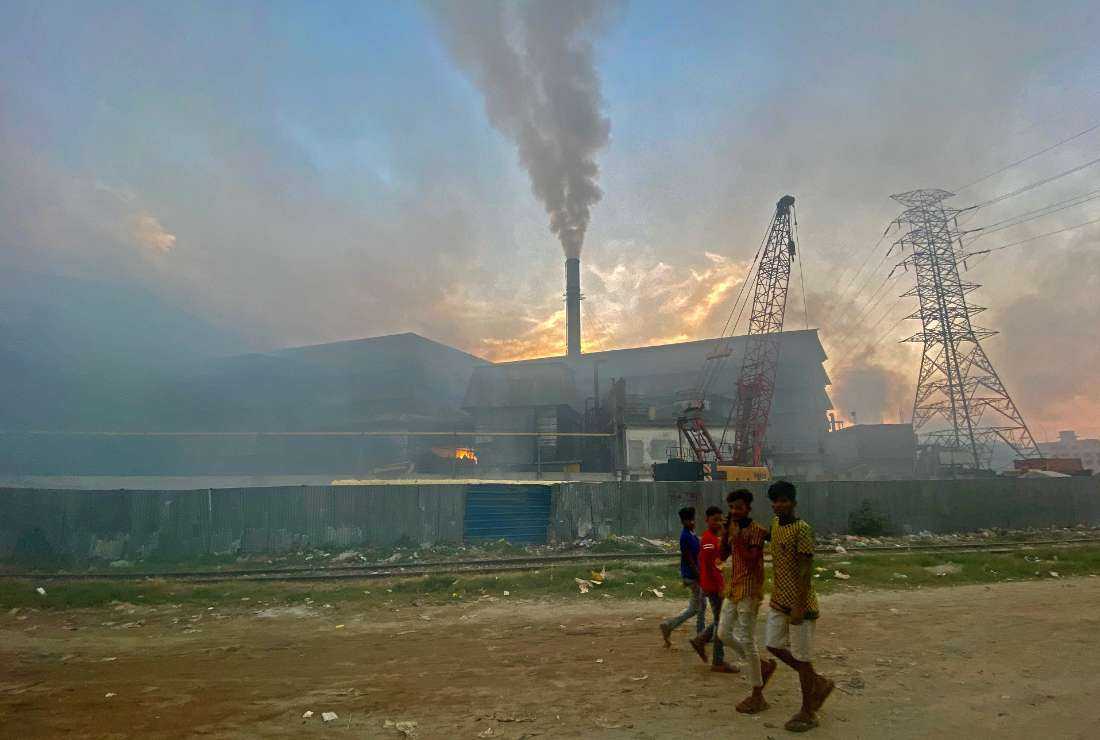 Commuters make their way to work as smokes rises from the chimney of a steel re-rolling mill in Narayanganj of Bangladesh on November 10, 2021