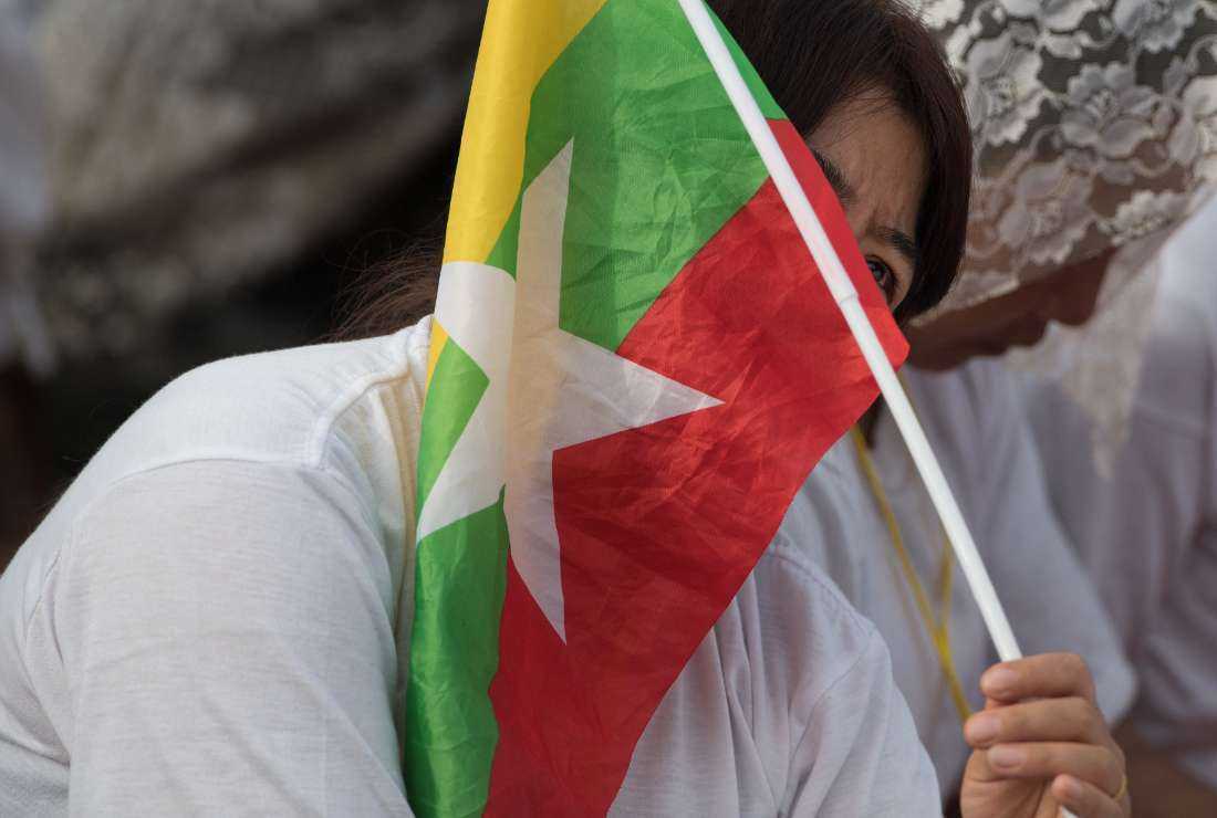 woman looks from behind a Myanmar flag while listening and watching Pope Francis on a large screen during an open-air mass in Yangon on Nov. 29, 2017
