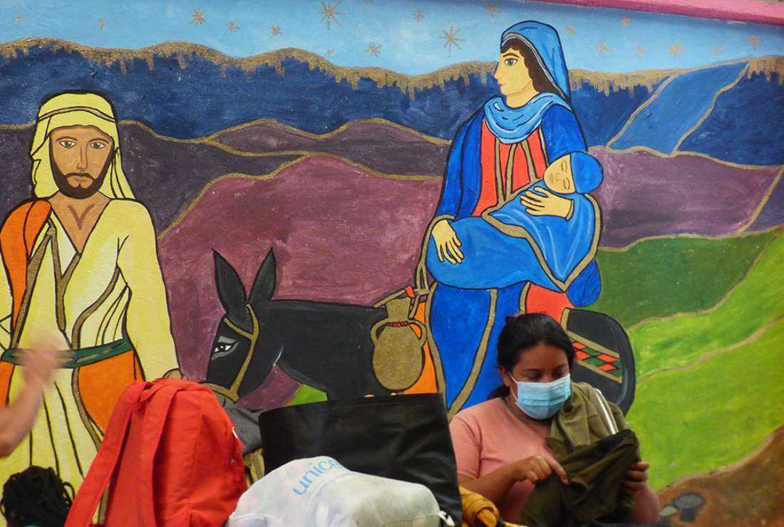 A woman gathers her belongings in front of a mural of Joseph and Mary at the CAFEMIN migrant shelter in Mexico City, Aug. 24