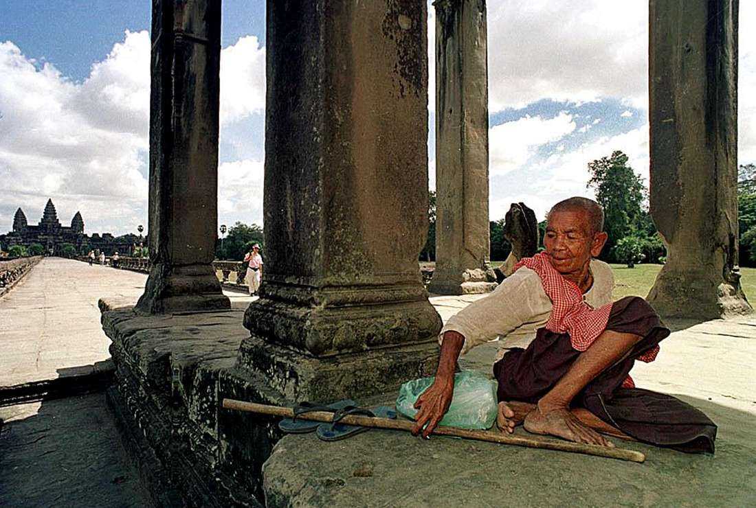 An elderly Cambodian woman installs her possessions in the shade of a temple in Angkor Wat as she waits for tourists to beg for money on Nov. 29, 2000.