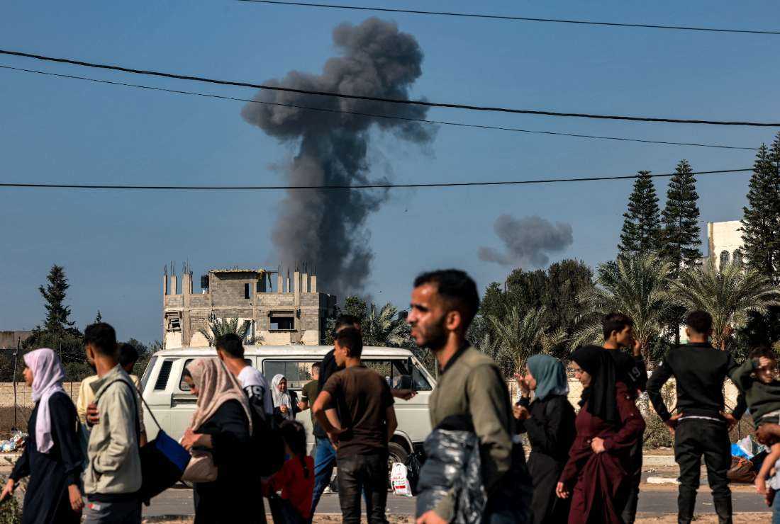 Smoke from Israeli bombardment rises behind people fleeing Gaza City and other parts of the northern Gaza Strip towards the south of the Palestinian enclave as they walk along a highway on Nov. 9.