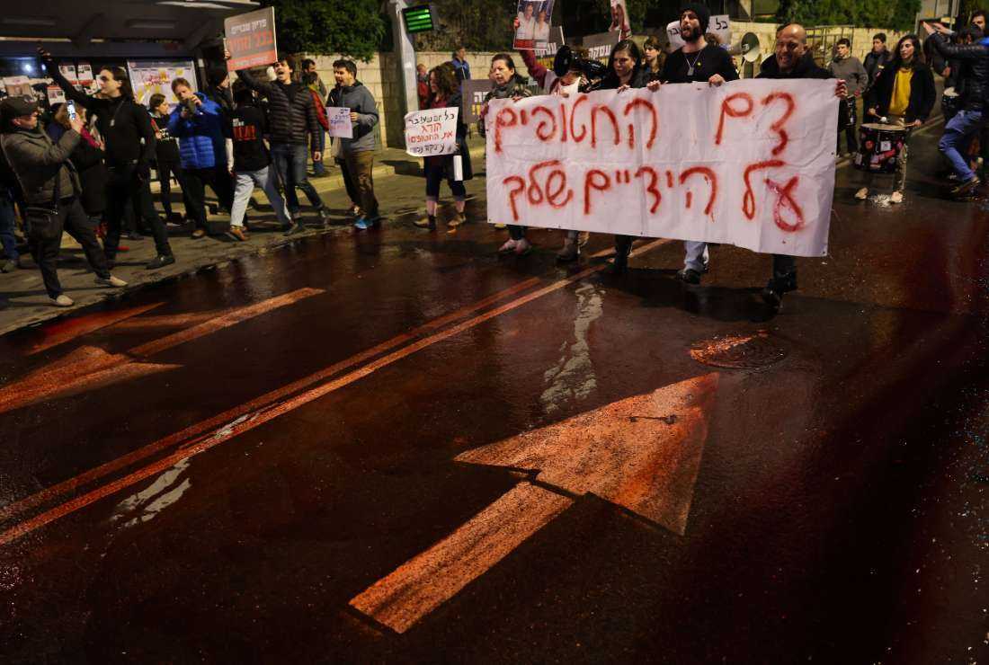 Protesters spill red paint on the road to symbolize the blood of the Israeli hostages in Gaza since the Oct. 7 attacks and carry a placard that reads 'the blood of the hostages is on your hands' during a rally calling for their release, on Jan. 22, 2024, near the residence of the Israeli prime minister in Jerusalem.
