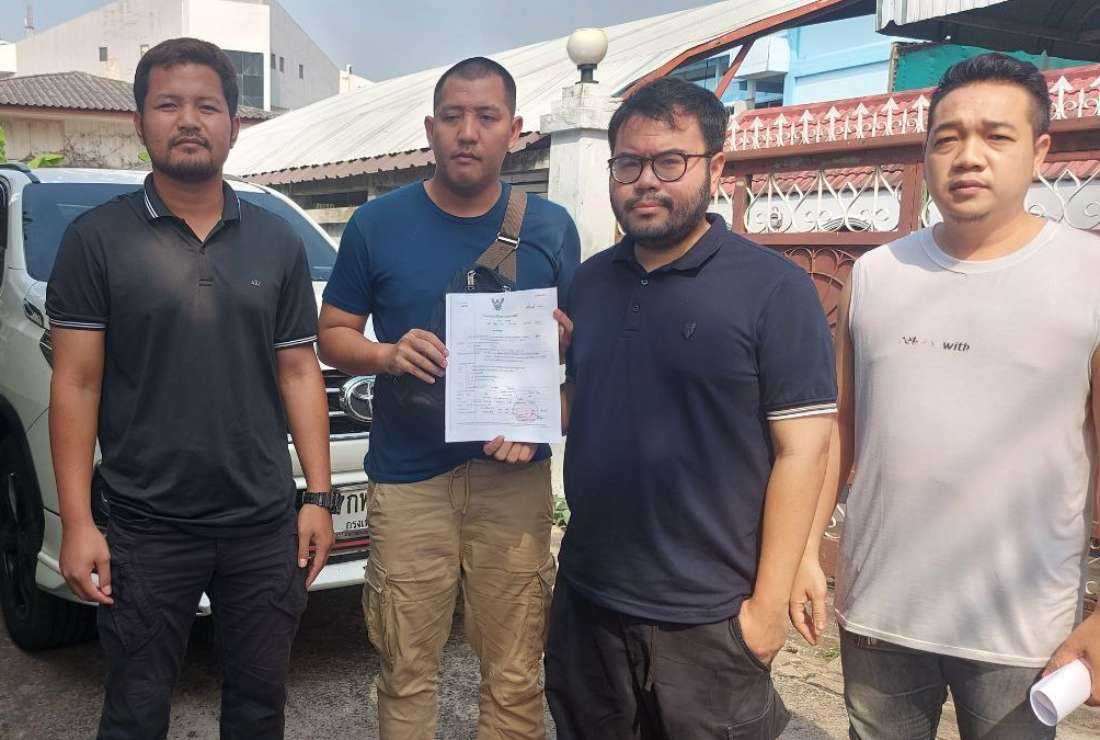 Nuttaphol Meksobhon (third from left) is handed an arrest warrant by police officers.