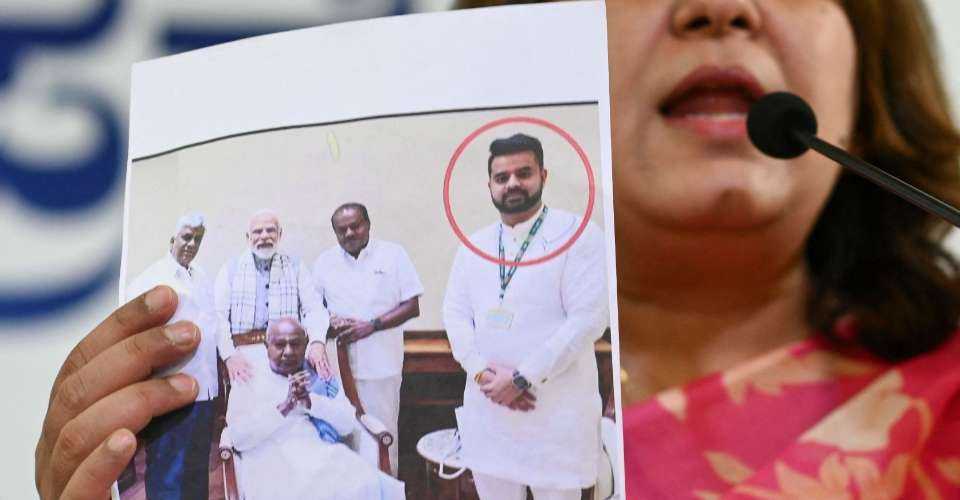 A Congress spokesperson shows a photograph featuring Indian MP Prajwal Revanna (in red circle) who was summoned for an alleged sexual abuse case, along with his family members and Prime Minister Narendra Modi (standing, second from left), at a press conference in Bengaluru on May 1.