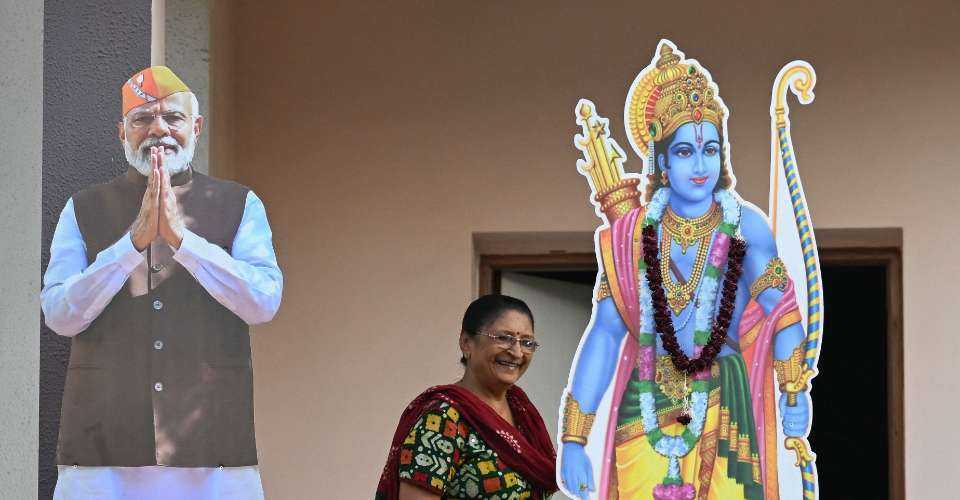 A woman stands on the balcony of a residential building with cut-outs of India's Prime Minister Narendra Modi and Hindu god Ram, in Ahmedabad on May 6