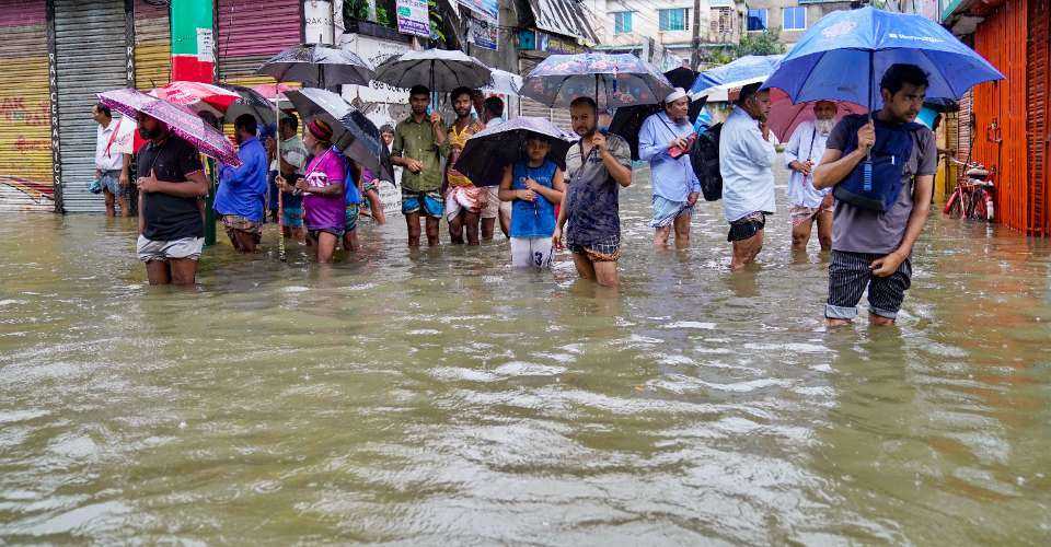 People carrying umbrellas, wade through a flooded street amid rainfall in Feni on Aug. 22. 